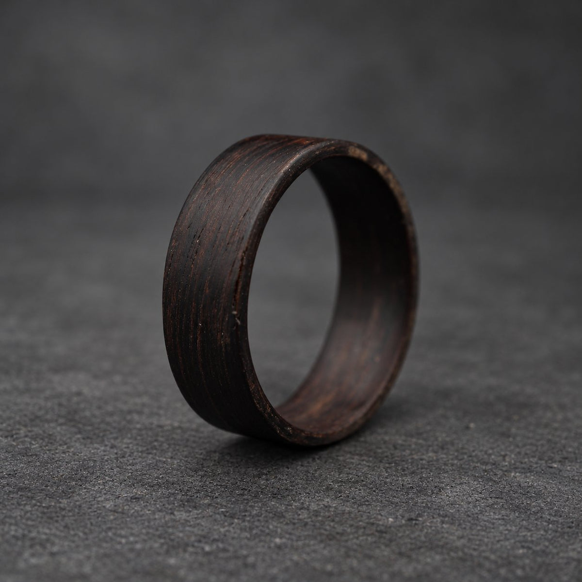 A black wooden ring with a smooth, polished finish. The ring is thick and has a wide band.