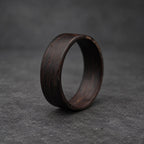 A black wooden ring with a smooth, polished finish. The ring is thick and has a wide band.