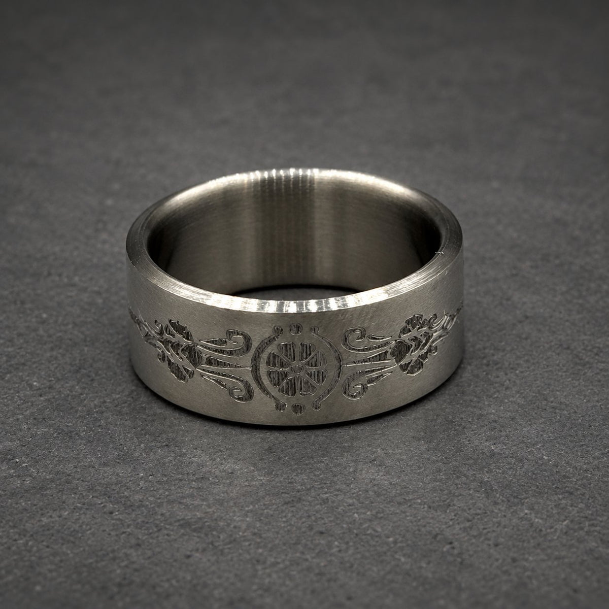 A silver ring with an engraved floral and geometric pattern. The ring is wide and has a smooth, polished finish. The design is centered and symmetrical.