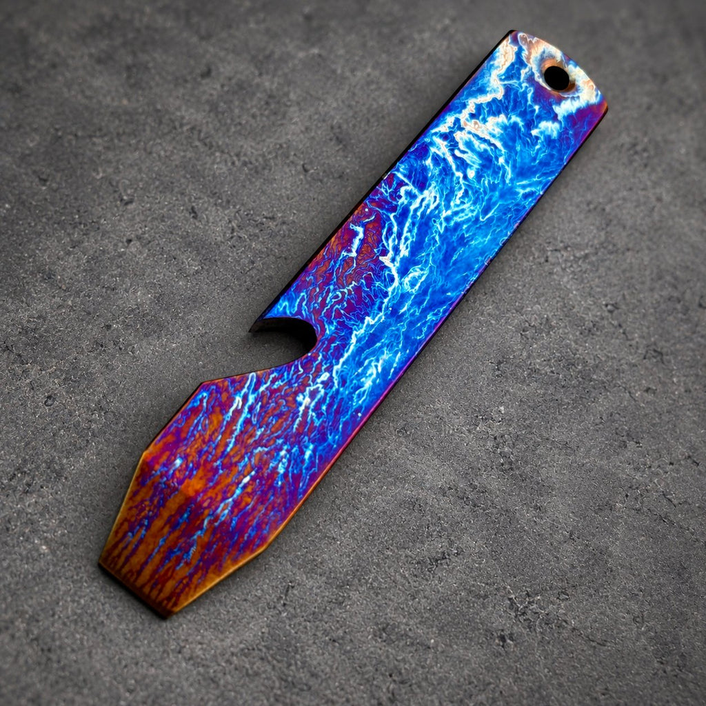 A striking bottle opener with a distinctive design. The opener showcases a blue and white pattern, reminiscent of lightning, blending into orange and purple tones. It has a hole at the top for hanging, with a length of approximately 10 cm.