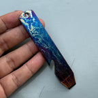 A multi-colored, rectangular bottle opener with a key ring hole. The opener features a blue, purple, and gold marbled design. The bottom of the opener has a bottle-opening notch.