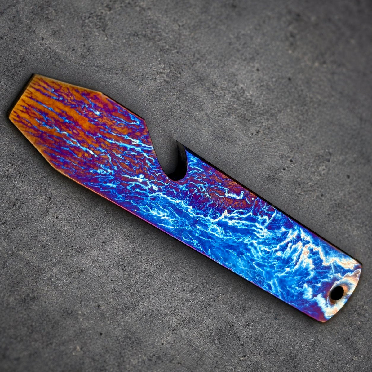A striking bottle opener with a distinctive color scheme. The opener displays a pattern of orange, blue, and purple, reminiscent of a stormy sky. It includes a bottle cap opener and a small hole.