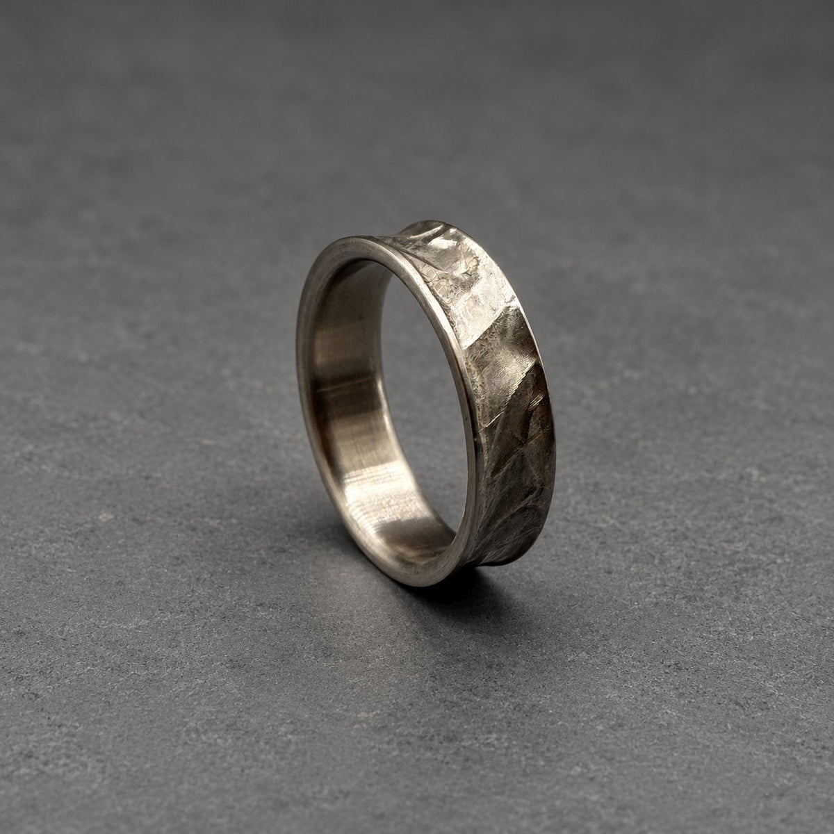 A silver ring with a textured, hammered finish. The ring has an irregular shape and a band approximately 0.6 cm wide. The surface has a rugged, industrial aesthetic, with visible hammer marks.