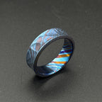 A patterned ring in shades of blue, purple, and orange. The ring has a textured surface and a band design. The ring is made of metal and is a striking piece of jewelry.