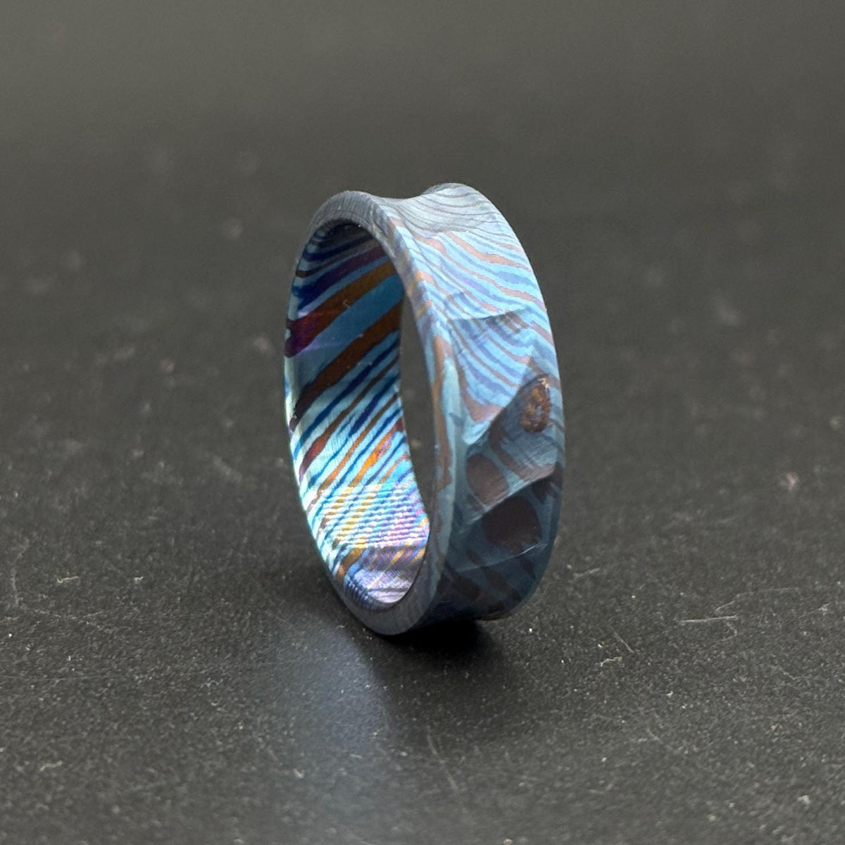 A distinctive ring with a textured surface and a layered, colorful design. The ring features shades of blue, brown, and purple. The ring's interior has a striped pattern. The ring is a piece of jewelry.