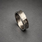 A silver ring with a textured, hammered finish. The band has an uneven surface with a slightly irregular shape. The ring is shown against a gray background.