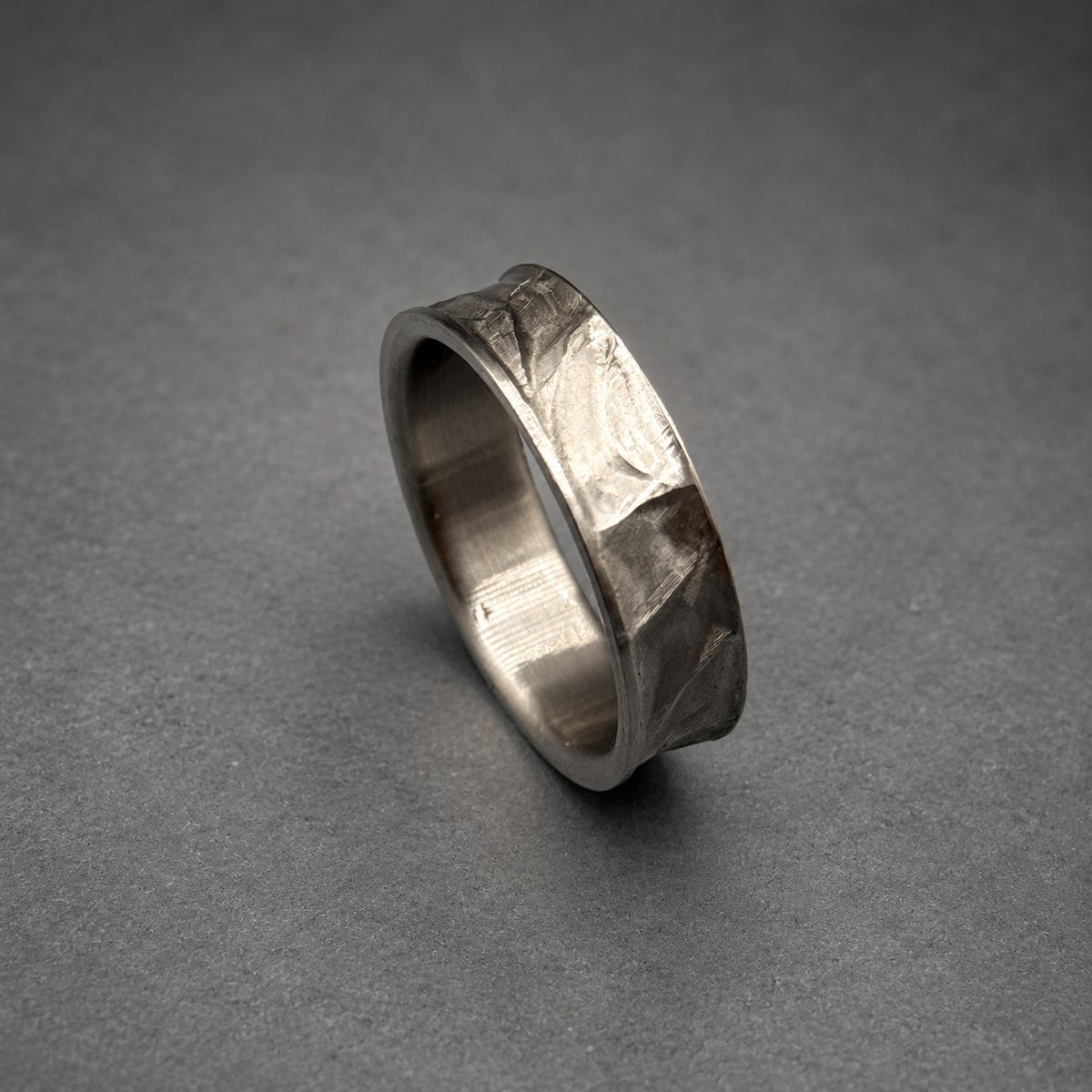 A silver ring with a textured, hammered finish. The band has an uneven surface with a slightly irregular shape. The ring is shown against a gray background.
