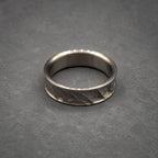 A silver ring with a textured band. The ring has a smooth inner surface and a patterned outer surface. The ring is displayed on a gray surface. Jewelry.