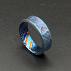 A patterned ring in shades of blue and purple. The ring has a distinctive wavy shape and a colorful interior with orange, blue, and purple stripes. The ring is made from a durable material and is suitable for everyday wear.