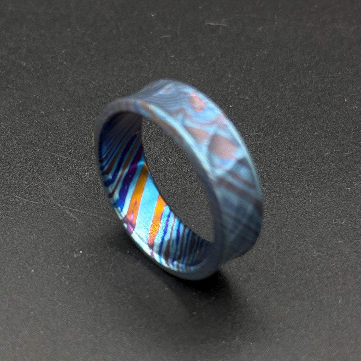 A patterned ring in shades of blue and purple. The ring has a distinctive wavy shape and a colorful interior with orange, blue, and purple stripes. The ring is made from a durable material and is suitable for everyday wear.