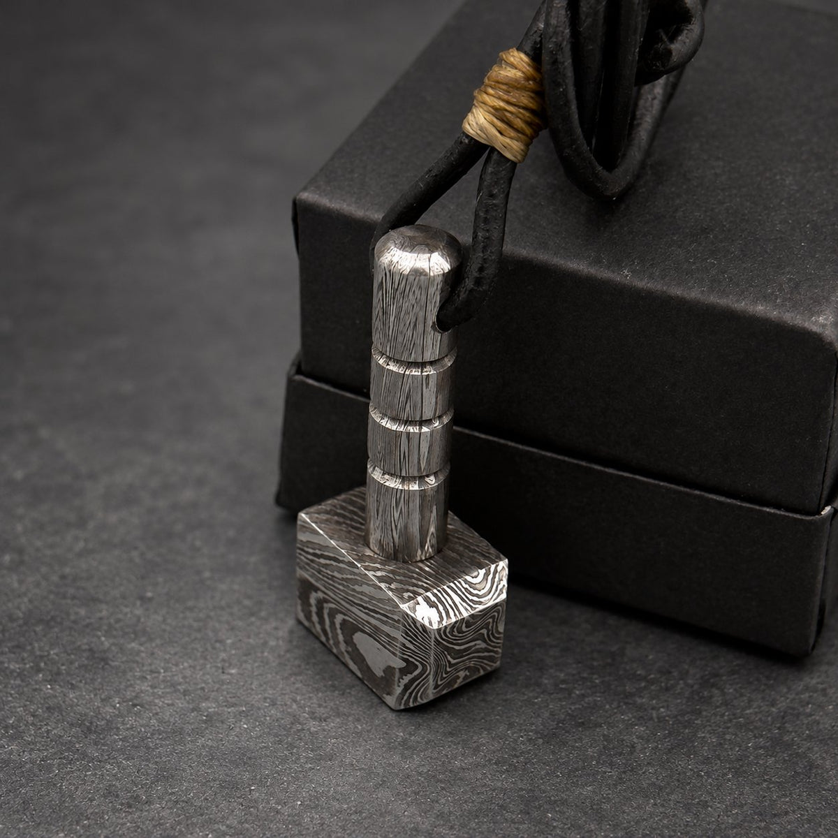 Damascus steel Thor hammer keychain standing upright against a black gift box