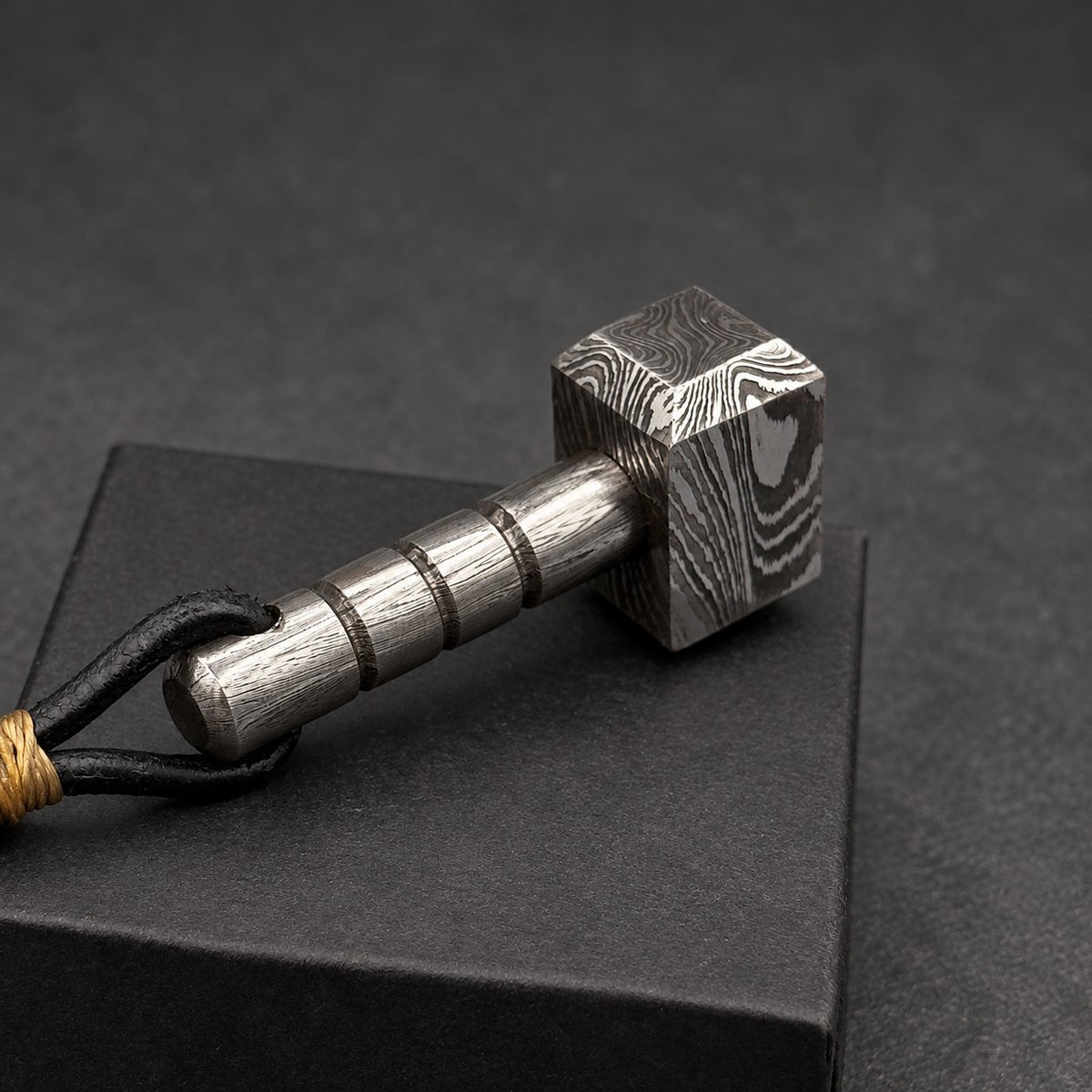 Damascus steel Thor hammer keychain angled across the corner of a black gift box