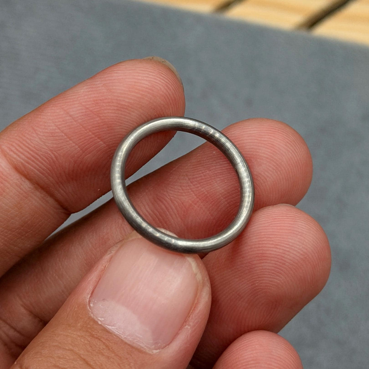 A close-up of a silver ring. The ring is a simple band with a smooth, metallic finish. The ring is held between fingers, showcasing its circular shape and polished surface. The ring appears to be made of metal.
