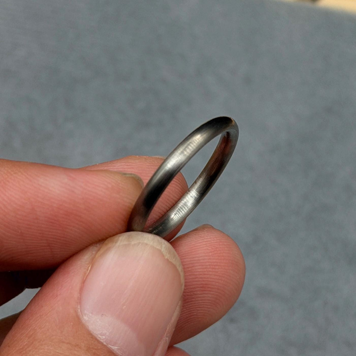 A silver ring with a smooth, rounded band. The ring is held between fingers, highlighting its simple, minimalist design. The ring appears to be made of metal and has a slightly worn appearance.