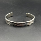 A silver cuff bracelet with a hammered texture. The open design allows for easy wear. The bracelet is a simple, yet stylish accessory.