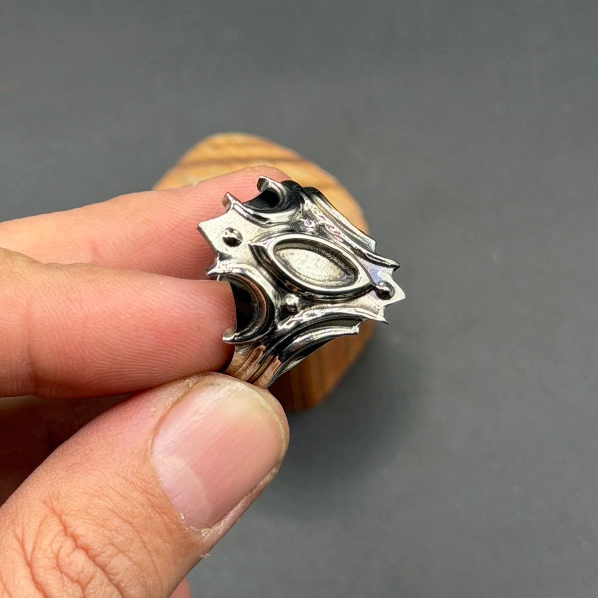 A silver ring with an elaborate, shield-shaped design. The ring has a central oval and multiple pointed edges, creating a bold and detailed aesthetic. The ring is held in a hand.