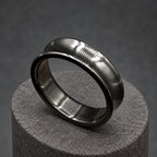 A black ear gauge, or plug, with a tunnel design. The gauge is made of a dark, shiny material and is circular with a flared shape. It is displayed on a wooden block. The gauge is designed to stretch the earlobe.