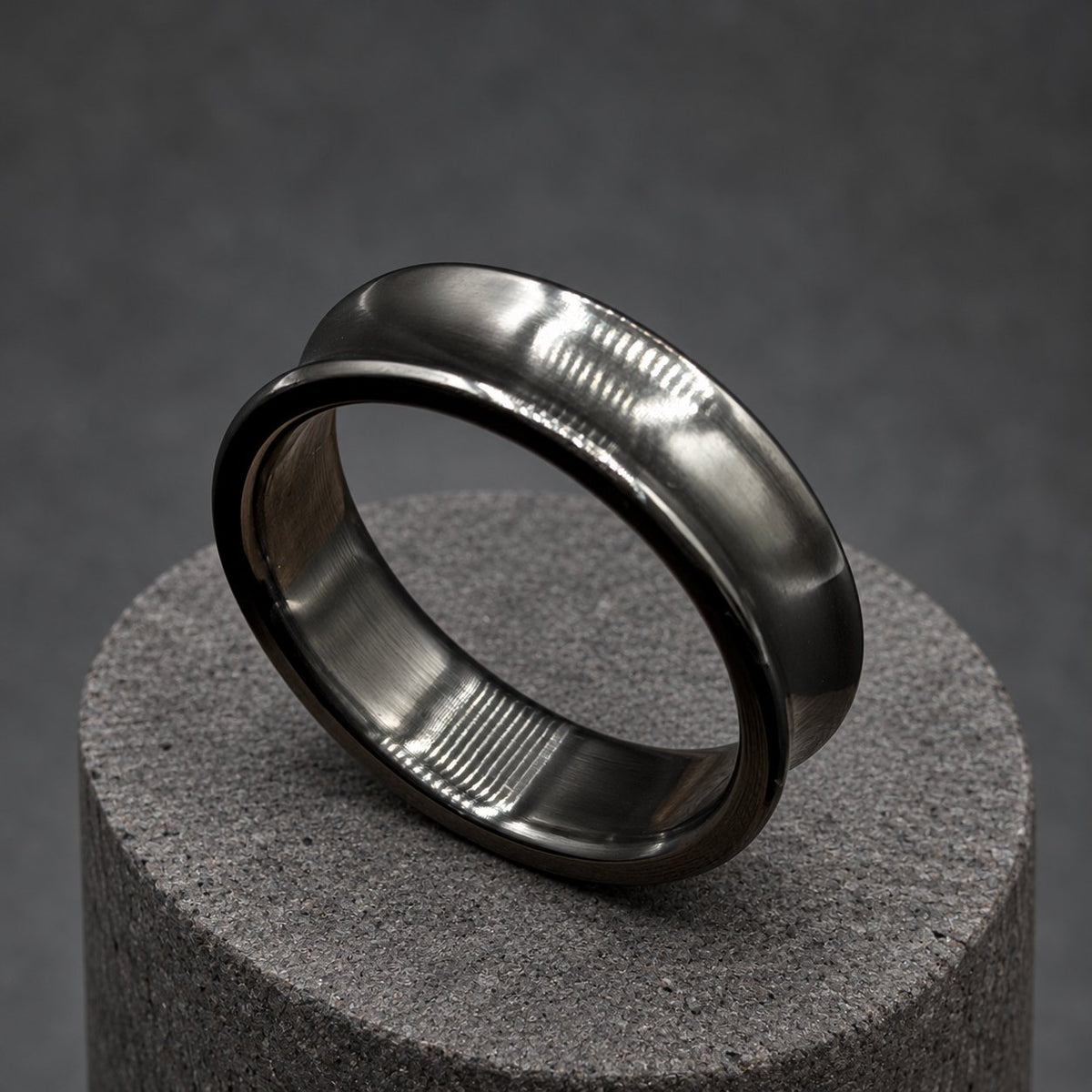 A black ear gauge, or plug, with a tunnel design. The gauge is made of a dark, shiny material and is circular with a flared shape. It is displayed on a wooden block. The gauge is designed to stretch the earlobe.
