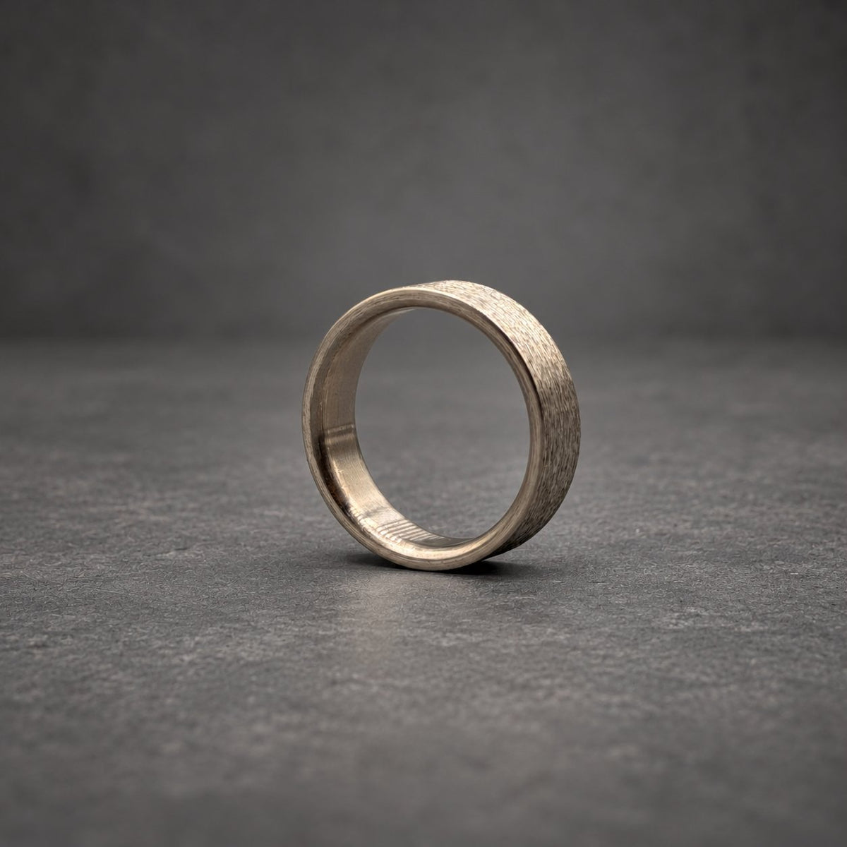 A circular ring with a metallic gray finish and a textured, brushed exterior surface. The band features a smooth, polished interior lining that contrasts with the rugged, matte appearance of the outer circumference of the ring.