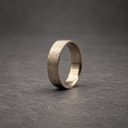 A silver-toned metal ring featuring a textured, brushed finish on the outer surface. The band has a consistent width and a smooth, polished interior, showcasing a metallic sheen that reflects light across its circular form.