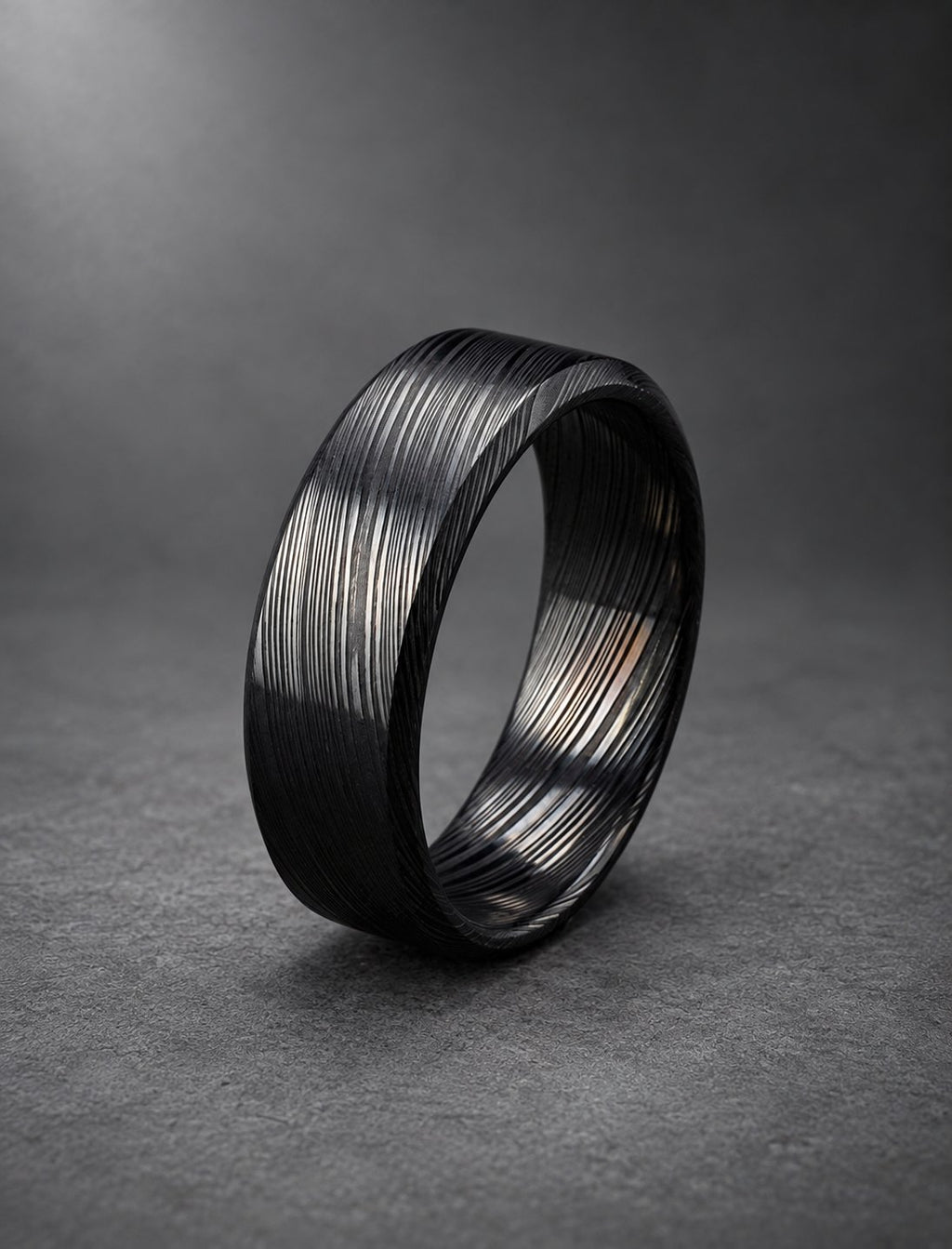 Black Damasteel wedding band with beveled bright edges, on dark stone