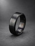 Black Damasteel wedding band with beveled bright edges, on dark stone