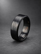 Black Damasteel wedding band with beveled bright edges, on dark stone