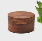 A round, dark brown wooden container with a matching lid. The wood features a visible, natural grain pattern throughout the cylindrical body and the flat top surface, showcasing a smooth, polished finish on the exterior of the object.