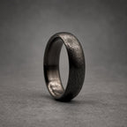 A dark gray ring with a textured, matte finish on the exterior surface. The band has a rounded profile and a smooth, polished interior surface, showcasing a consistent dark metallic appearance throughout the entire circular structure.