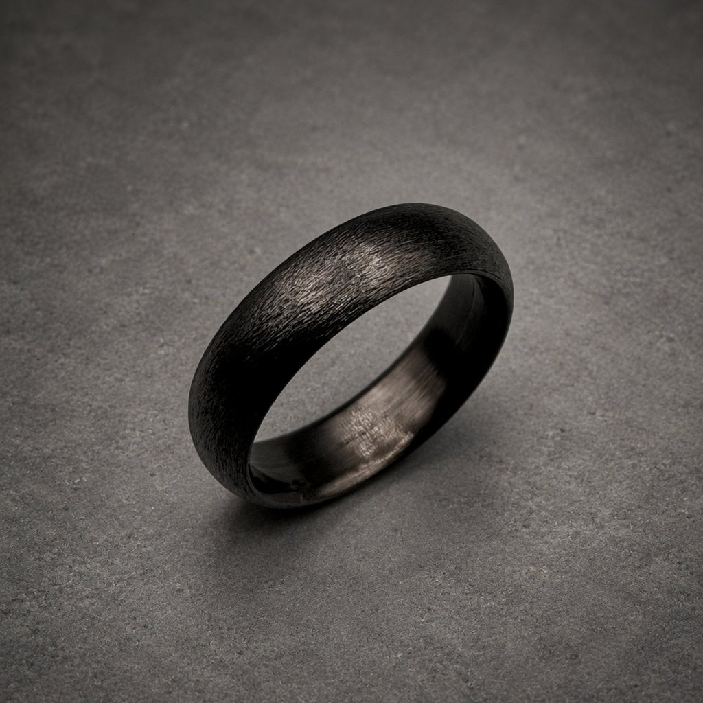 A dark charcoal gray ring with a textured, brushed finish on the outer surface. The band has a rounded profile and a smooth, polished interior. The metal appears matte and dark, showing fine horizontal striations across the exterior.