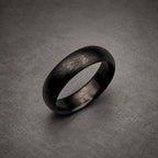 A dark charcoal gray ring with a textured, brushed finish on the outer surface. The band has a rounded profile and a smooth, polished interior. The metal appears matte and dark, showing fine horizontal striations across the exterior.