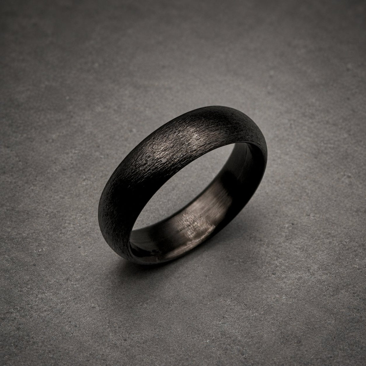 A dark charcoal gray ring with a textured, brushed finish on the outer surface. The band has a rounded profile and a smooth, polished interior. The metal appears matte and dark, showing fine horizontal striations across the exterior.