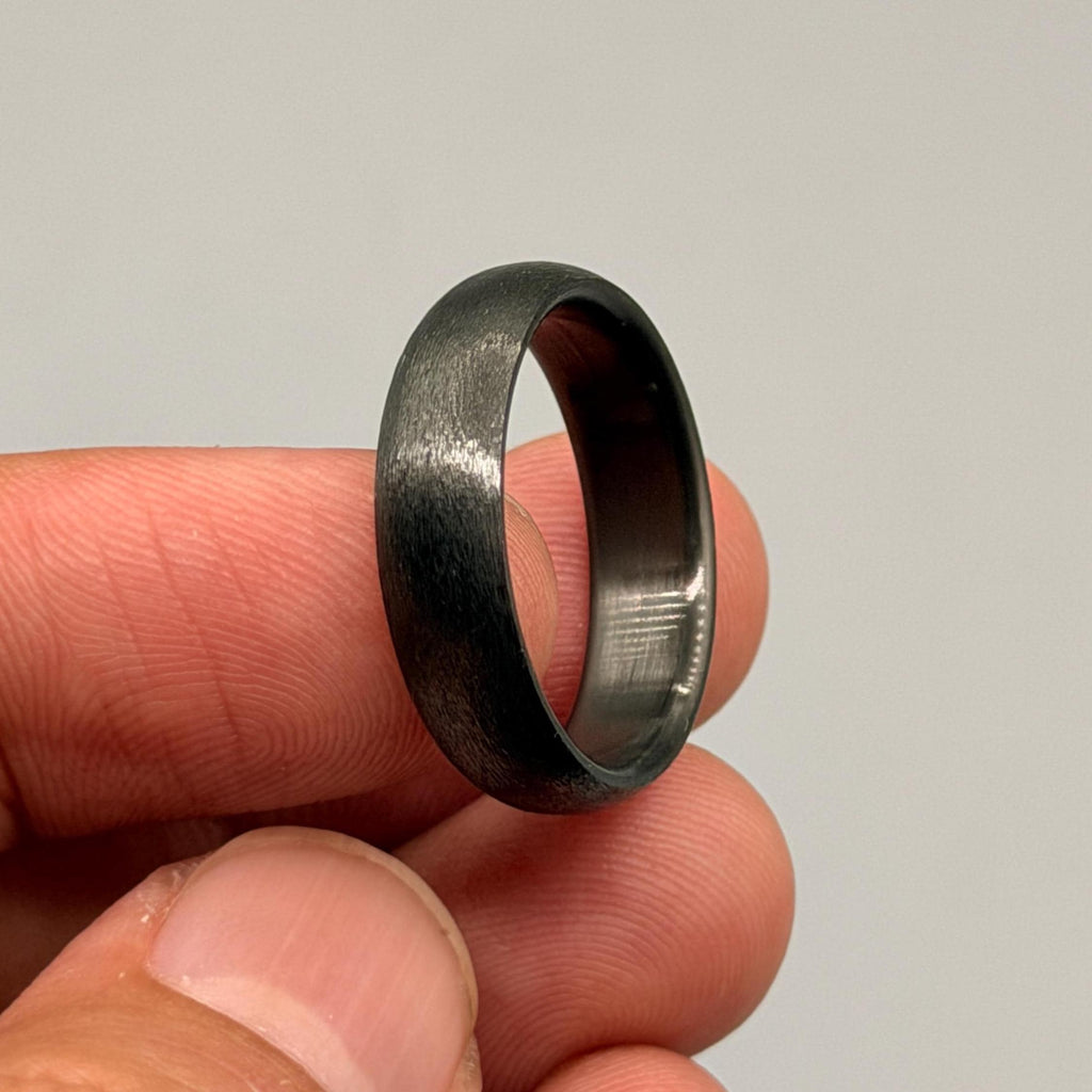 A dark gray ring with a brushed, textured finish on the exterior surface. The band features a smooth, polished interior surface that contrasts with the matte, weathered appearance of the outer metal band.