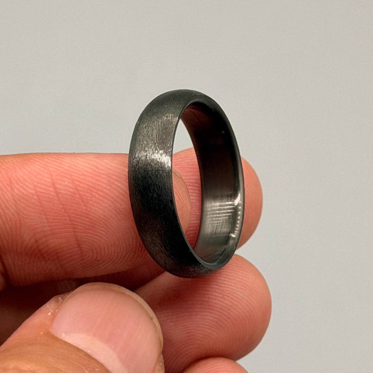 A dark gray ring with a brushed, textured finish on the exterior surface. The band features a smooth, polished interior surface that contrasts with the matte, weathered appearance of the outer metal band.