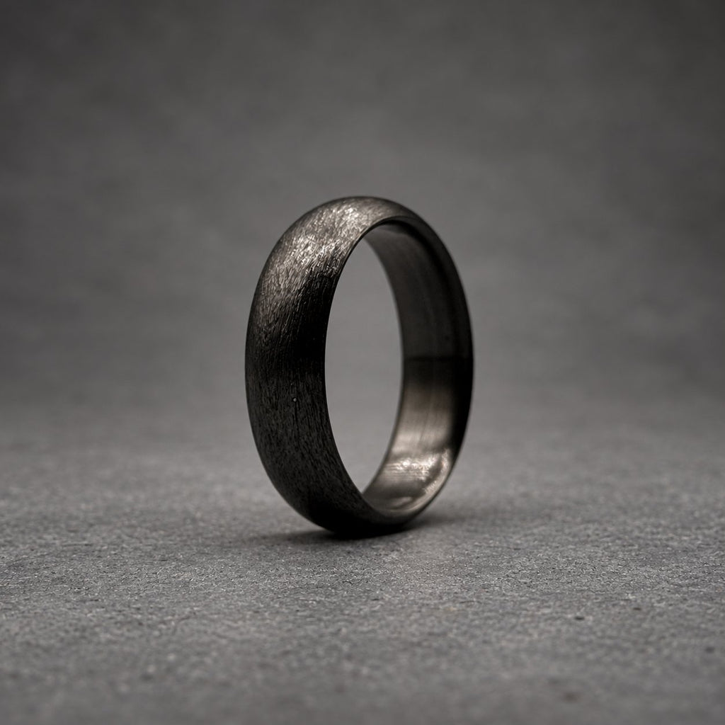 A dark gray ring with a textured, matte finish on the outer surface and a smooth, polished interior. The band has a rounded profile and a consistent width throughout, showcasing a deep charcoal color with subtle variations in the surface texture.