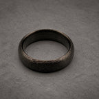 A circular ring with a dark charcoal gray color and a textured, matte finish. The band has a consistent width and a smooth, polished interior surface that contrasts with the rough, granular appearance of the outer circumference.