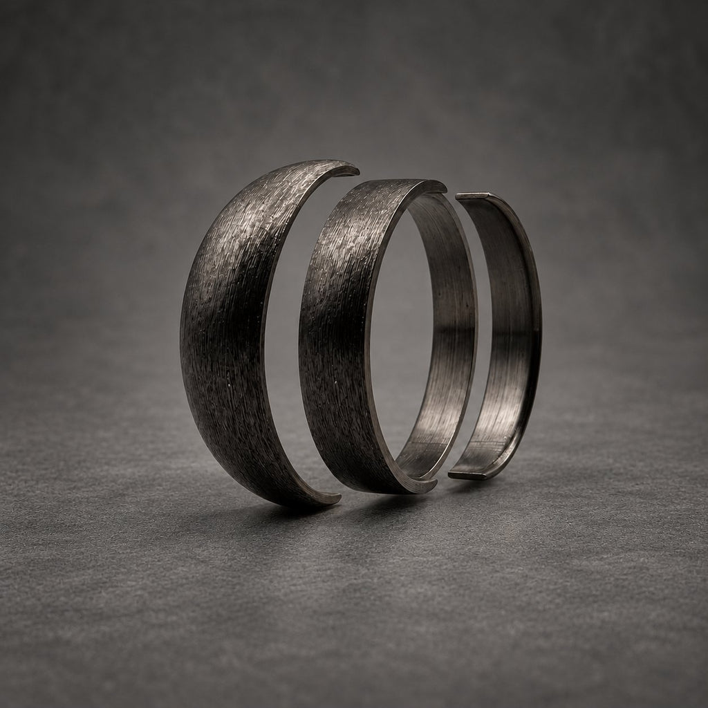 Three dark gray rings arranged in a row, each featuring a textured, brushed metal finish. The rings are positioned vertically, showing a consistent matte appearance across their curved surfaces, creating a layered visual effect.
