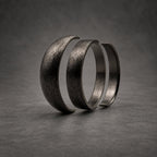 Three dark gray rings arranged in a row, each featuring a textured, brushed metal finish. The rings are positioned vertically, showing a consistent matte appearance across their curved surfaces, creating a layered visual effect.